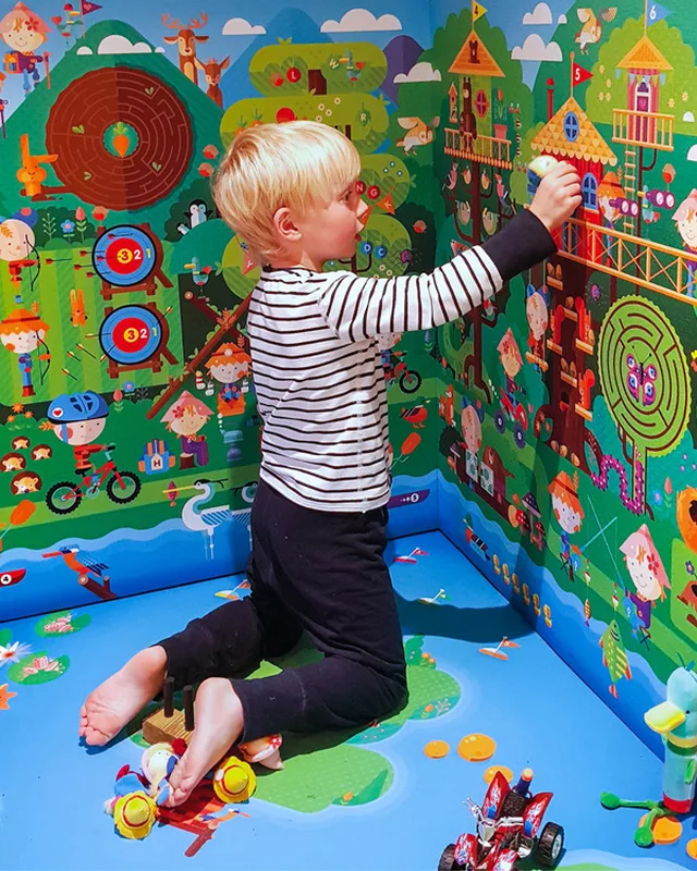 Kind spielt an einer bunten Wand voller illustrierter Figuren und Wege