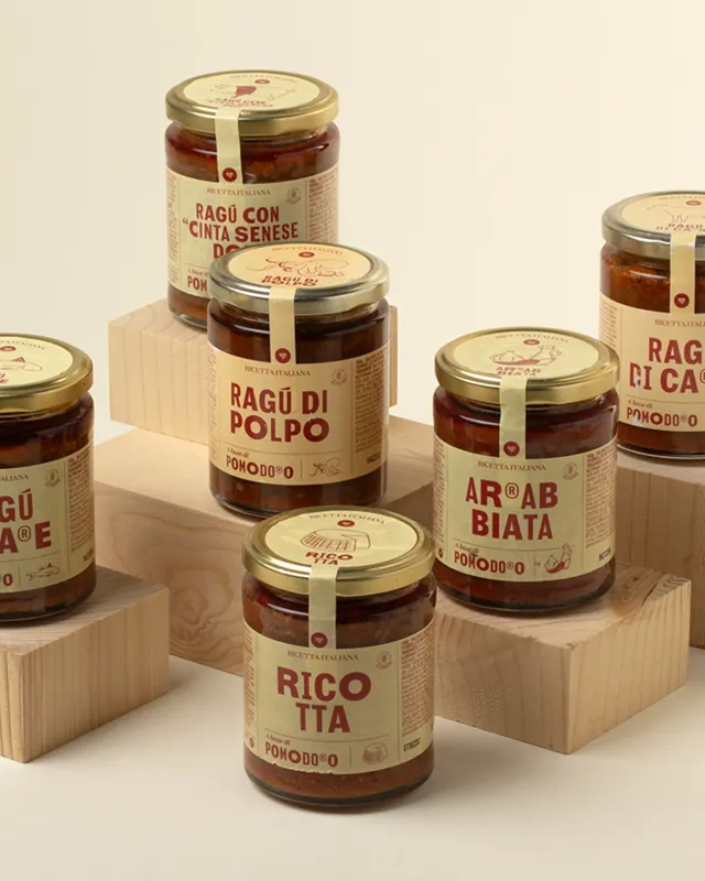 Mehrere Gläser mit Tomatensaucen und rot-beigen Etiketten auf Holz